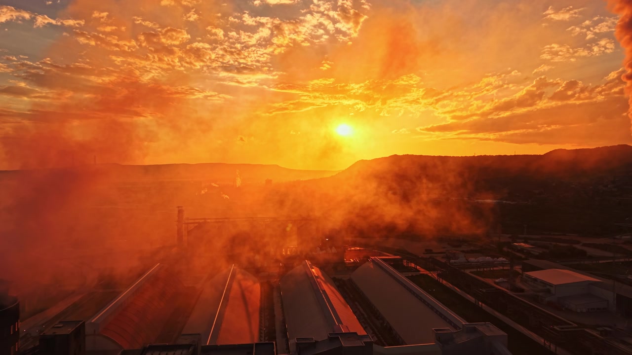 Sunset view over industrial area with smoke and clouds in the sky creating an orange glow during evening hours