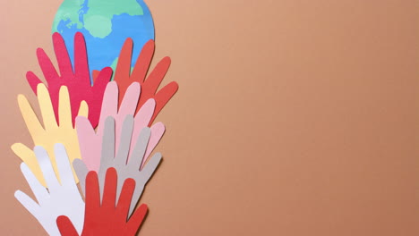Close up of hands together with globe made of colourful paper on brown background with copy space