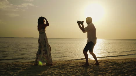 silueta de un fotógrafo masculino en la playa que está fotografiando a una mujer joven 4k video