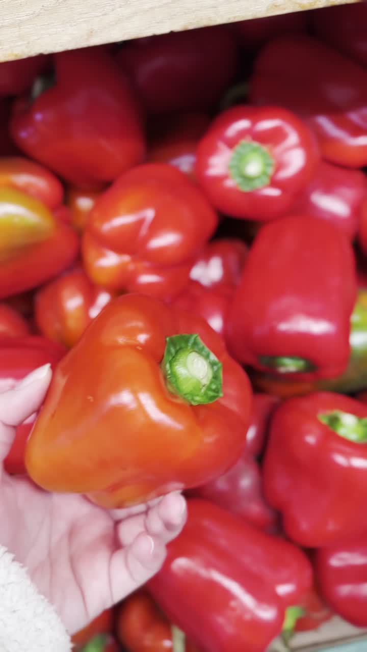 Hand picking red bell peppers from a store display