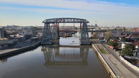 4K-Aerial-tracking-shot-across-the-Riachuelo-Matanza-river-capturing-Puente-Transbordador-Nicolas-Avellaneda-bridge-and-Buenos-Aires-downtown-cityscape-on-a-tranquil-sunny-day