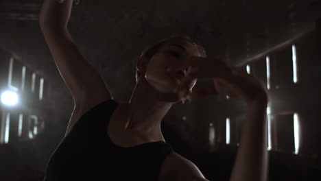 Close-up-of-ballet-dancer-as-she-practices-exercises-on-dark-stage-or-studio.-Ballerina-shows-classic-ballet-pas.-Slow-motion.-Flare-gimbal-shot.