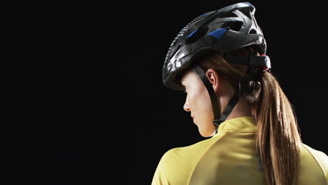 young caucasian woman cyclist in cycling gear, with copy space on black background