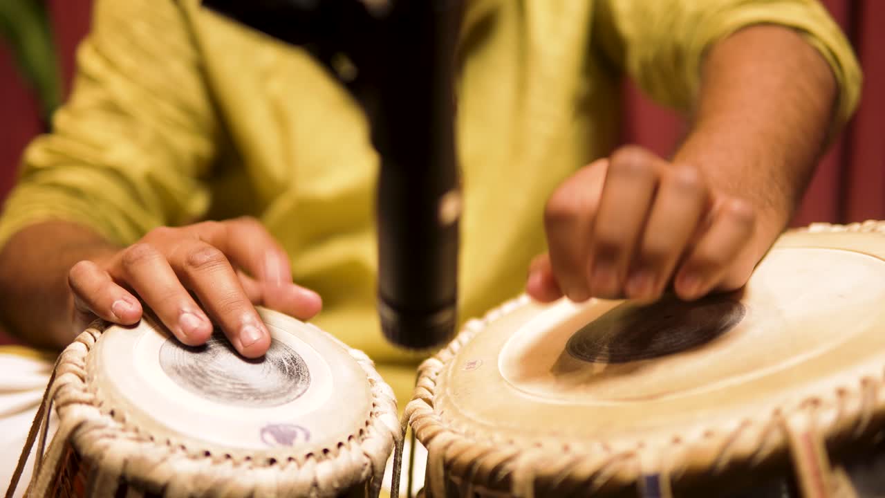 Primer plano de un artista tocando la tabla, destacando la percusión tradicional india, el ritmo y la interpretación de música cultural con un movimiento detallado de las manos sobre la superficie del tambor.