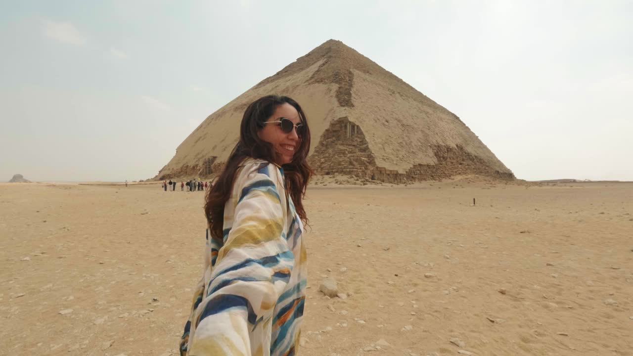 Donna che tiene la mano e cammina verso un'antica piramide nel deserto egiziano