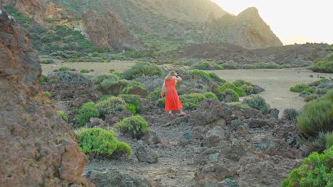 tourist in orange dress carefully walks in rocky volcanic landscape