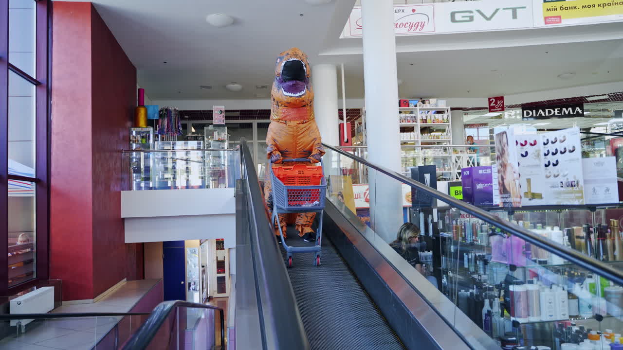 Funny dinosaur going by the escalator with shopping cart. Animator in orange spotty costume doing shopping in the modern mall.