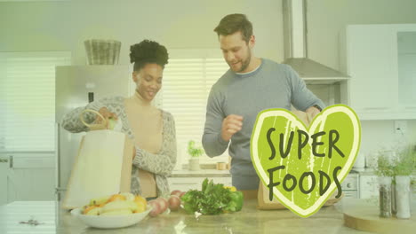 animation of super foods text over diverse couple preparing healthy meal in kitchen