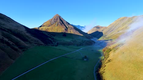 aerial view of a serene mountain valley with mist rolling over lush green fields, captured in early morning light