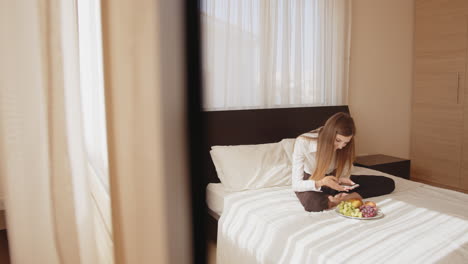 mujer relajándose en la cama con desayuno y teléfono