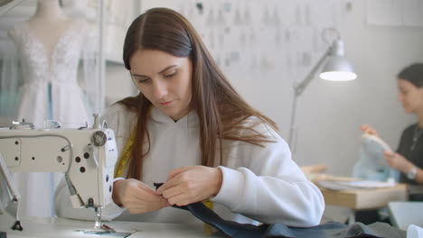 teamarbeit von zwei schneider und schneider, die lächeln und an der nähen einer neuen kollektion arbeiten. die näherin schneidet das muster mit einer schere und der stylist folgt dem arbeitsablauf