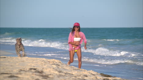 fit latin girl running on the beach playing with her dog schnauzer enjoying a sunny afternoon smiling and having fun