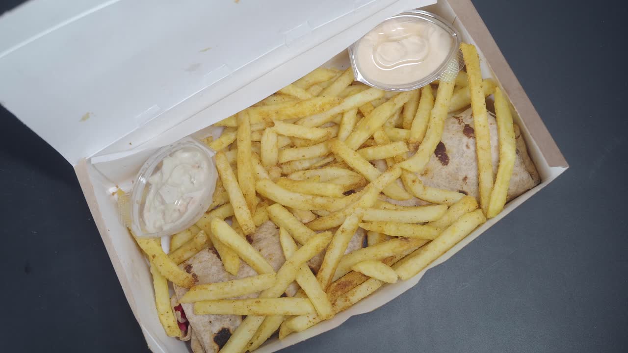 Primo piano di un ordine di cibo in una scatola con patatine fritte e due salse.