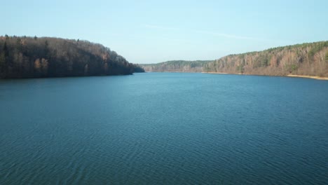 aerial: flying over gorgeous blue lake and green forest in autumn day