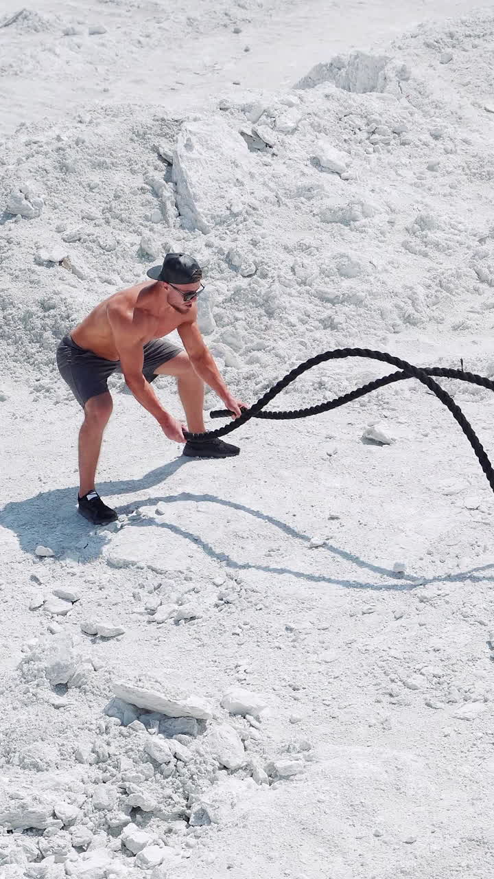 Male bodybuilder doing intense athletic exercises with ropes. Training on the nature on white sand. Vertical video