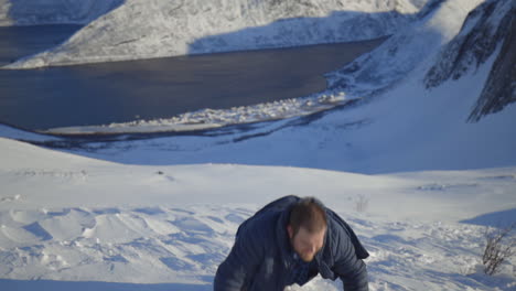 an exhausted man struggles to stand up after reaching the top of a snowy mountain