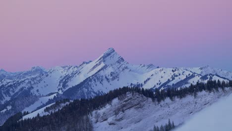 captivating aerial view showcasing the tranquil silhouette of a snow-covered mountain range at sunrise, filmed by drone