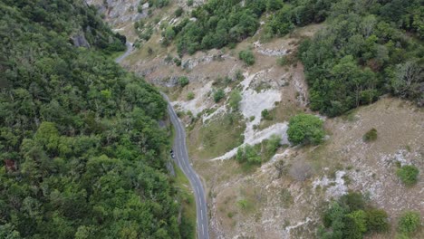 aerial view following a car travelling down a road twisting through the limestone cliffs at cheddar gorge in the mendip hills, uk with dense lush forest on one side and grassy rocks on the other