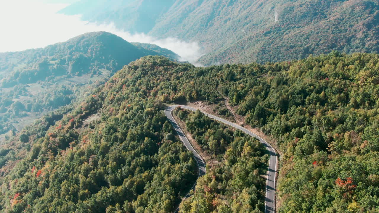 Mountain road with trees alongside it Other mountains can be seen in the distance The road twists and turns