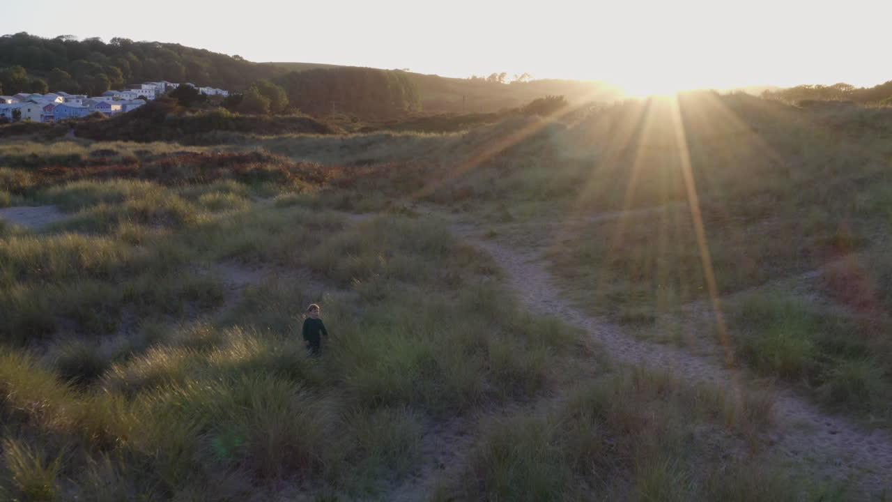 tomada de un dron de niños jugando en dunas de arena en la playa de invierno cuando se pone el sol