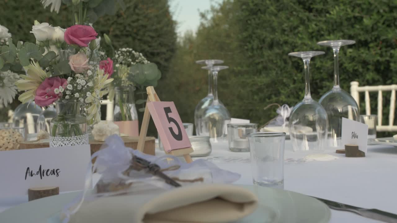 Manos colocando copas de vino en una mesa de boda mientras se prepara la mesa de recepción al aire libre.
