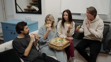 fecha doble. felices amigos masculinos y femeninos tomando una deliciosa pizza sentados en el sofá