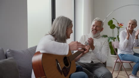 happy senior woman singing and playing the guitar raising hand, while her elderly friends clapping