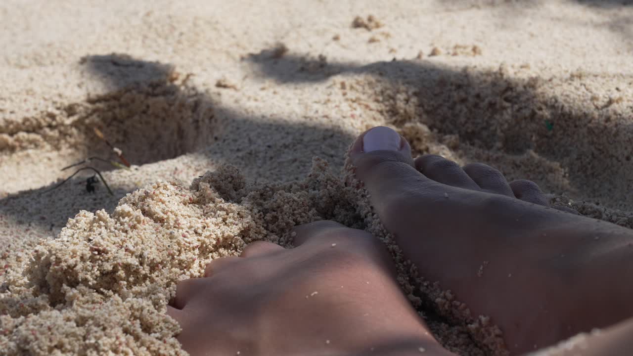 Small woman feet with gel pedicure in soft beach sand, up-close