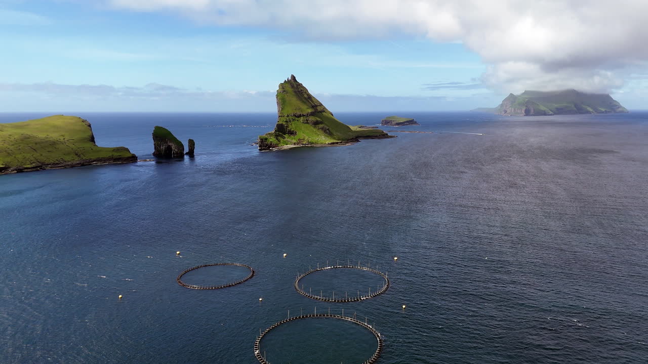 Cinematic aerial view of Drangarnir sea stacks rising dramatically from the Atlantic Ocean near Vágar, Faroe Islands, showcasing rugged cliffs, lush green slopes, and misty Nordic seascape