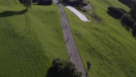 a vertical drone shot of cyclists scattered along a winding road between barns and green fields in tyrol.