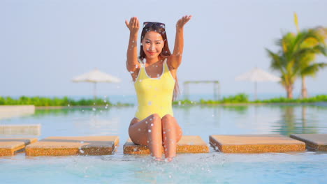 a happy playful young woman splashes pool water into the air