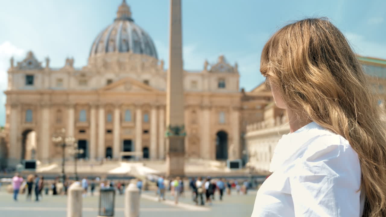 Visuale da dietro di una donna bionda nella Città del Vaticano. Piazza San Pietro con numerosi turisti, Basilica di San Pietro e l'obelisco vaticano sullo sfondo. Rallentatore