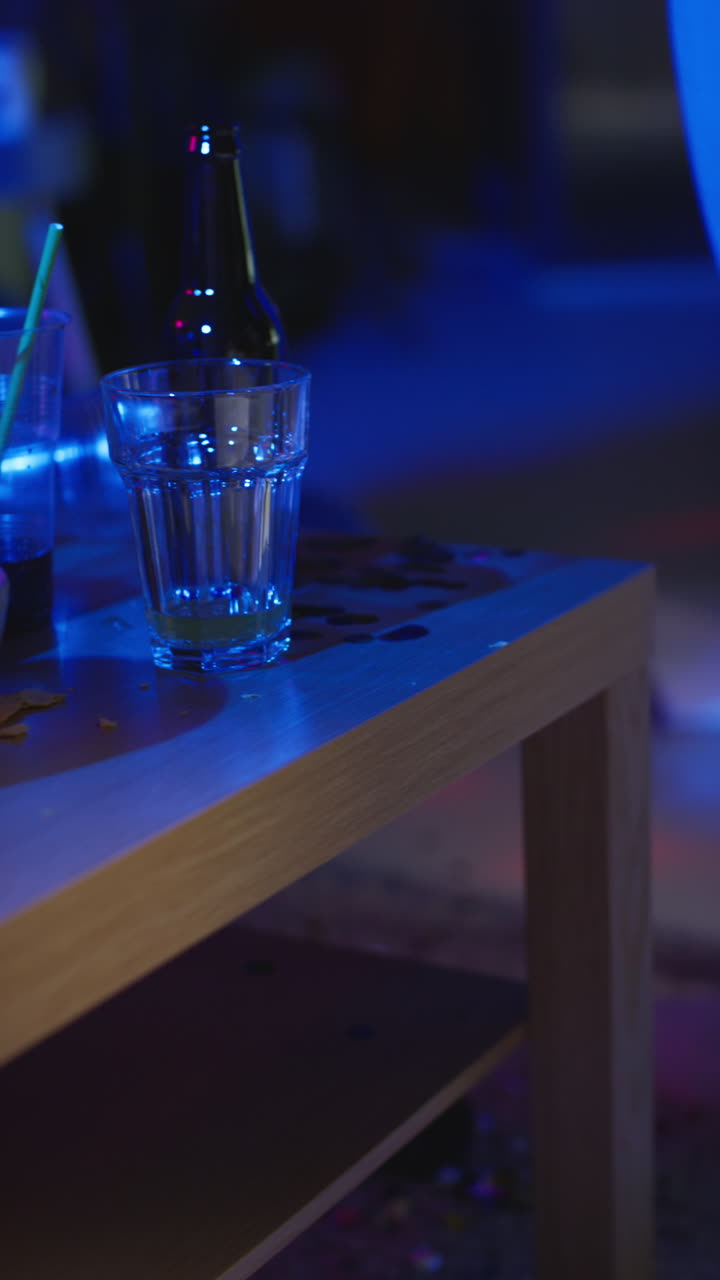 video vertical de primer plano de una mesa desordenada cubierta con vasos de vino vacíos botellas de cerveza y bocadillos en la fiesta de la casa