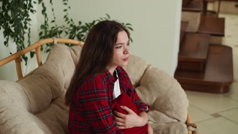 young woman sitting on a couch looking away, holding a red pillow