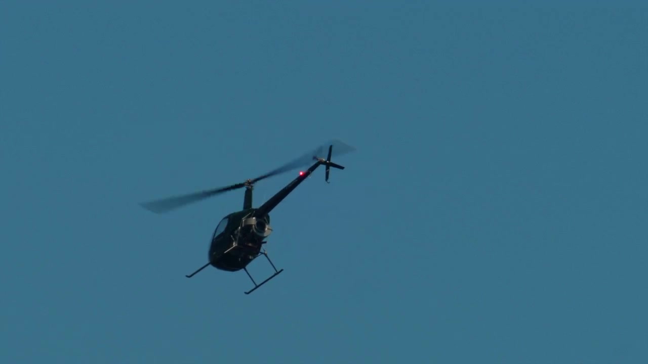 Hélicoptère noir avec des pales en rotation rapide volant dans un ciel bleu clair, illustrant le transport aérien et l'aviation, Antibes, France