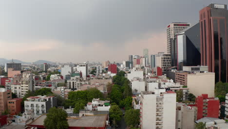 Forwards-reveal-of-low-residential-houses-neighbours-with-tall-office-buildings.-Low-flight-over-city-downtown.-Mexico-City,-Mexico.