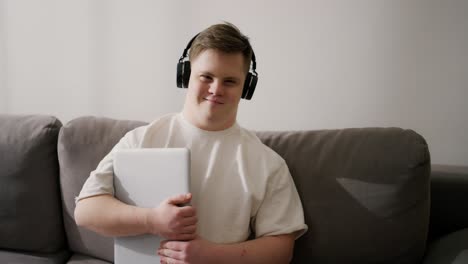 hombre con síndrome de down en casa con auriculares, sosteniendo una computadora portátil
