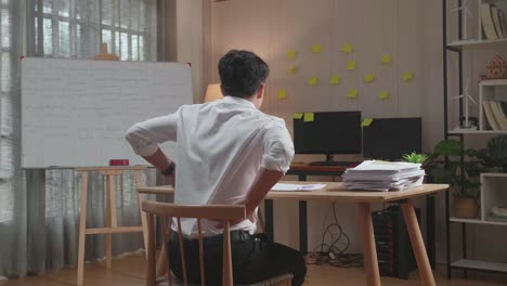 back view of asian man having backache while working hard with documents at the office