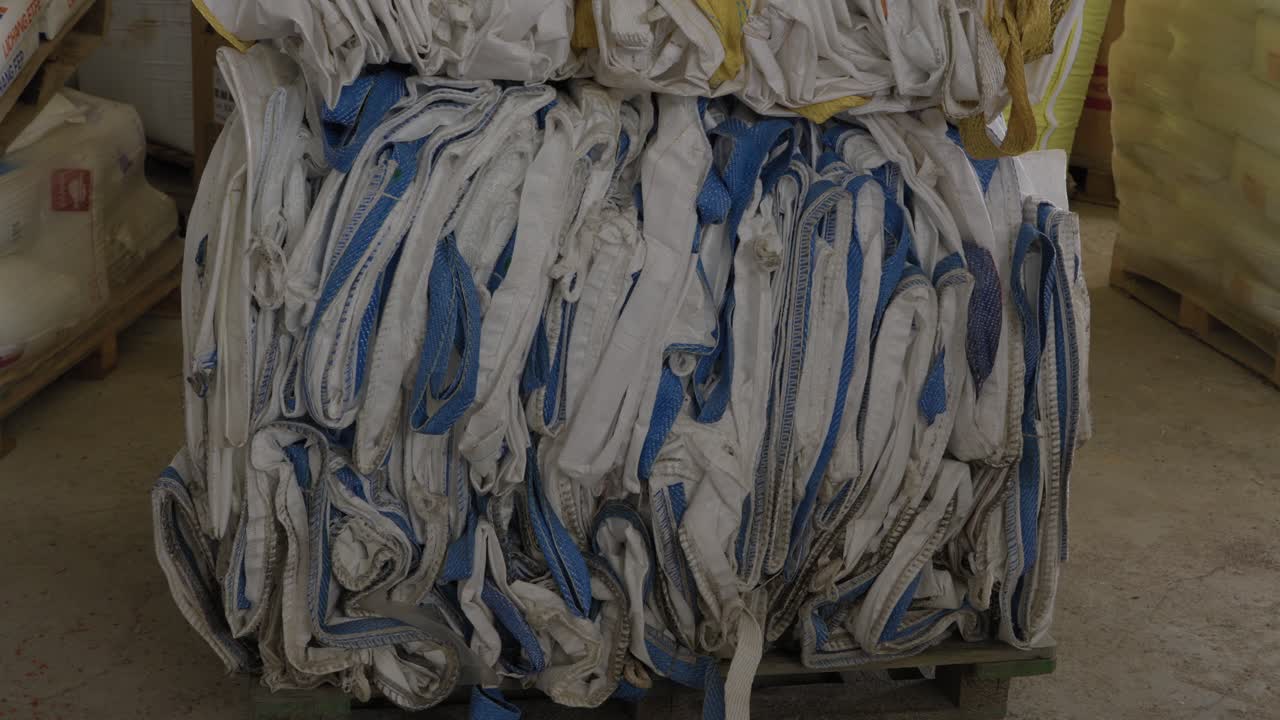 Stacked bale of crushed used woven polypropylene bags on pallet inside recycling facility