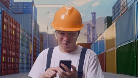 primer plano de hombre asiático trabajador con gafas de protección y casco de seguridad mirando el teléfono inteligente luego gritando meta celebrando mientras estaba de pie en el depósito de contenedores