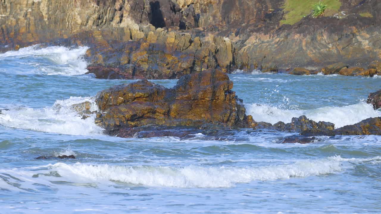 Dynamic ocean waves crash against rugged rocks under natural light at Charlesworth Bay Beach, creating a serene coastal scene