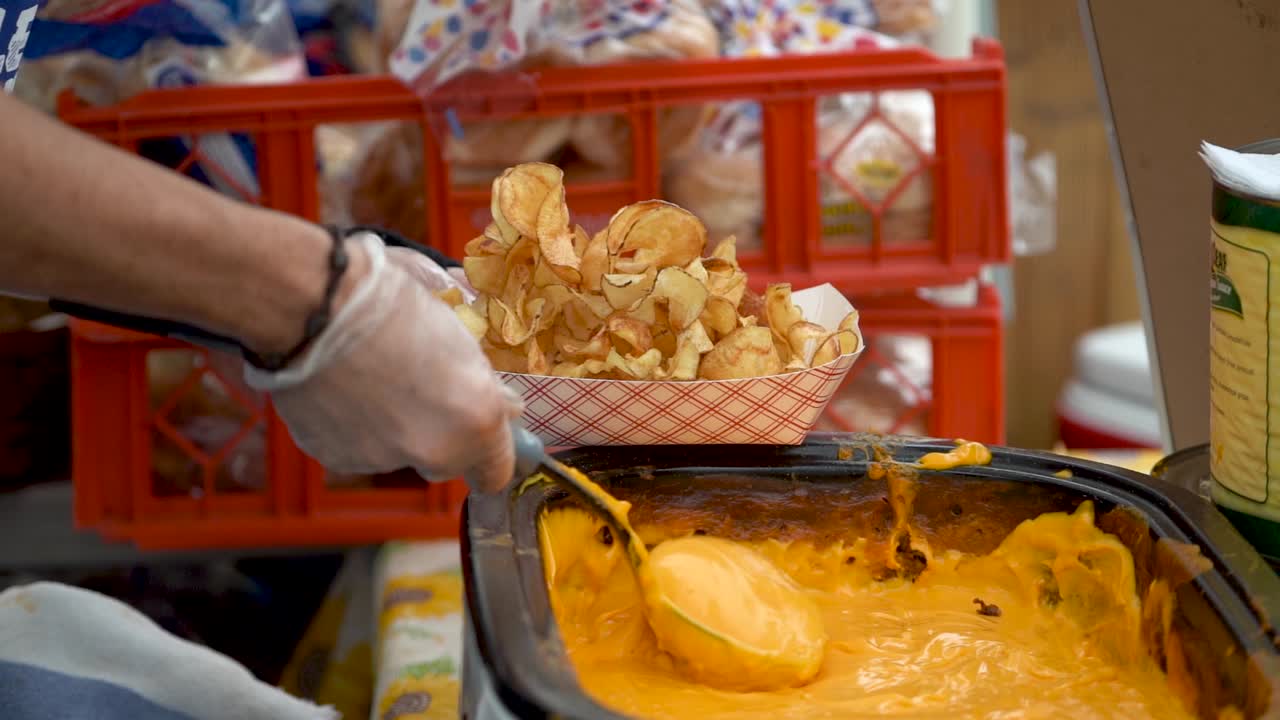 primer plano de cámara lenta de poner salsa de queso en una porción de tornado o papas fritas rizadas