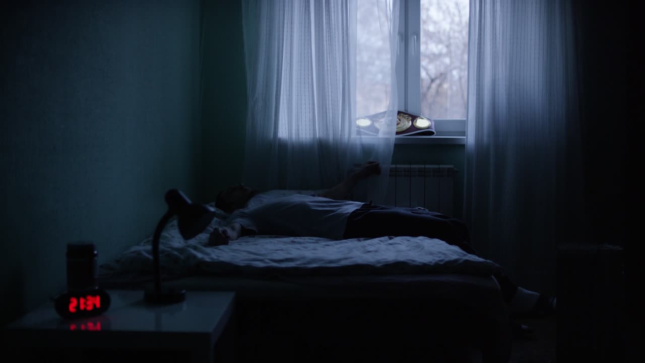 밤에 어두운 방에서 침대에 앉아 누워있는 남자