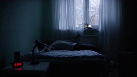 man sitting and lying on a bed in a dark room at night