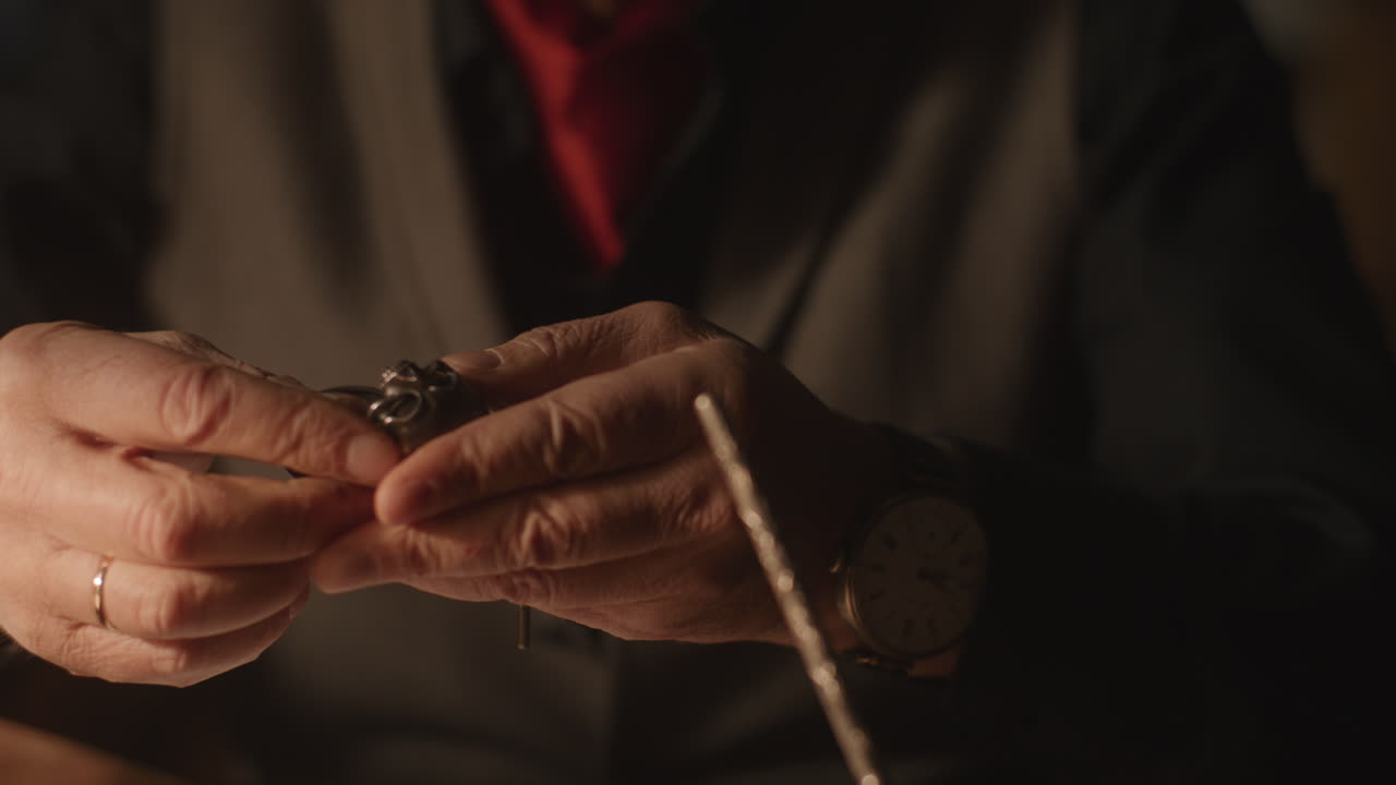 Older passionate man evaluates an old silver skull watch in his office at night