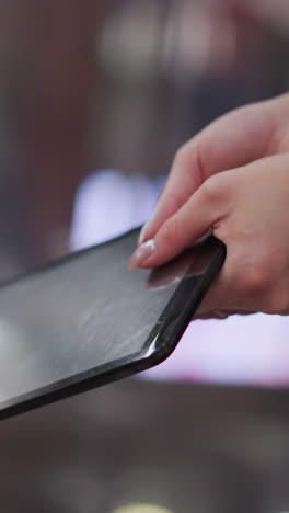 cerca de las manos con uñas pulidas balanceándose suavemente la tableta, mostrando sutiles reflejos de luz en la pantalla y un fondo colorido borroso