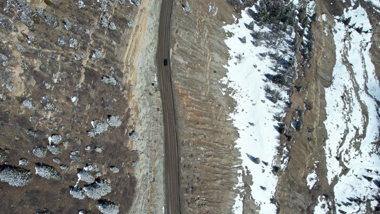Top Down Aerial View of Dark Car Moving on Countryside Road in Wilderness of USA on Winter Day