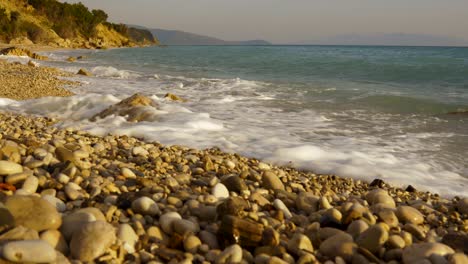 golden rocky beach with pebbles splashed by sea waves in mediterranean coastline