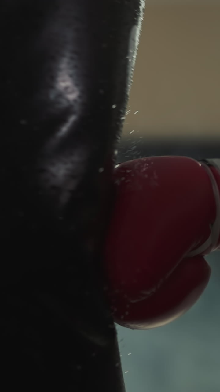 Boxing trainer hand in professional glove hits punching bag with power in gym with equipment. Male expert goes in for sports and gains muscle mass