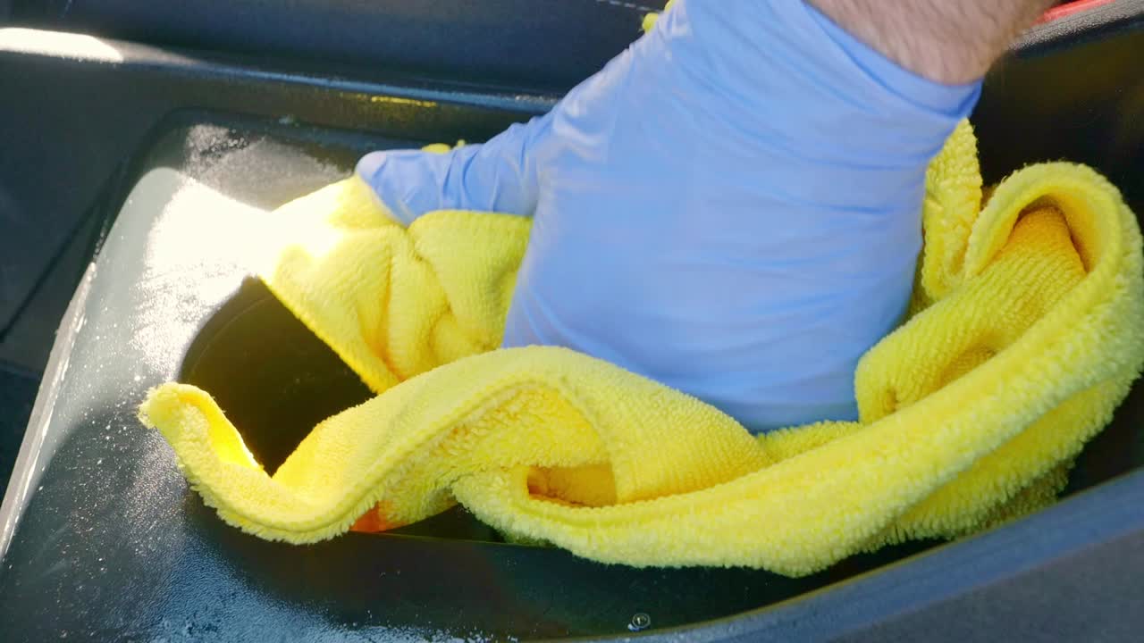Wiping away dirty product from cleaning car cup holders with yellow microfibre towel cloth - close up